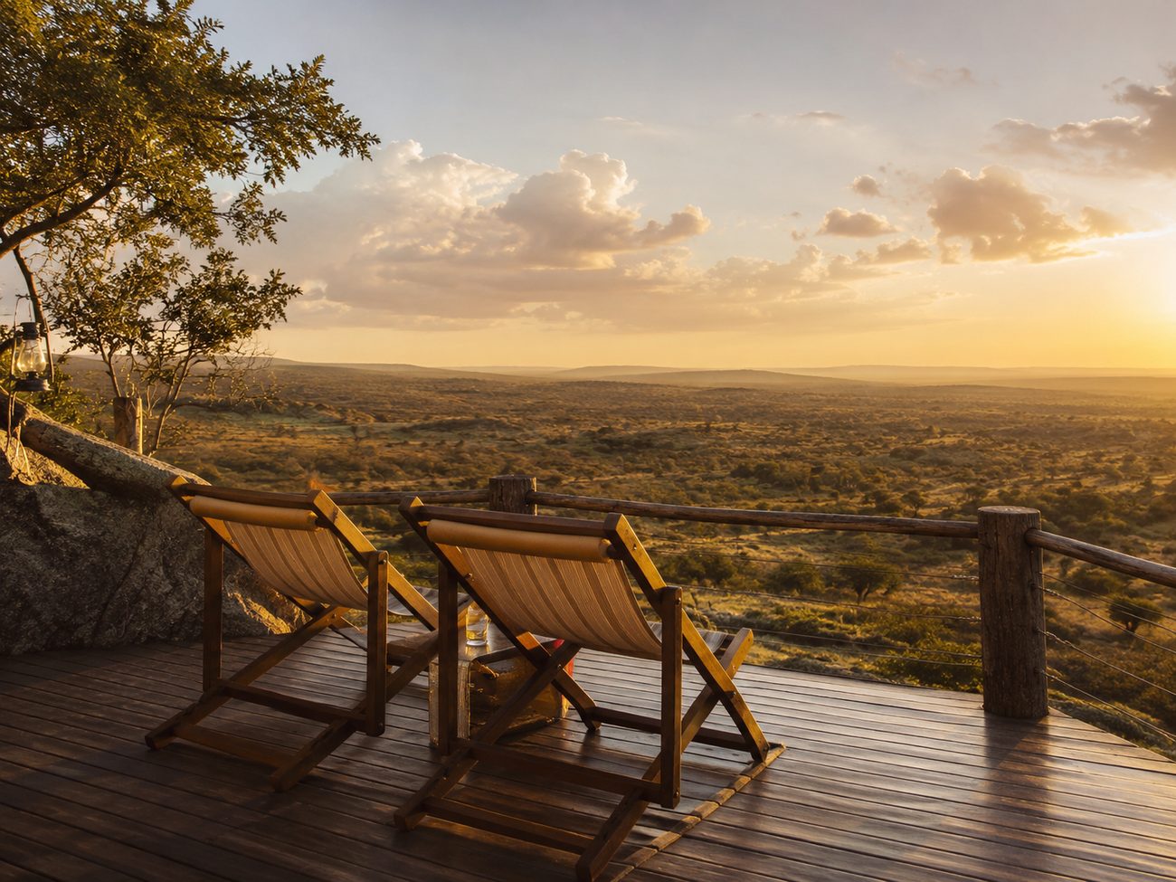 Two chairs on a safari lodge deck overlooking the plains at sunset